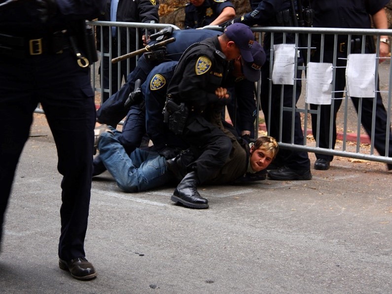 A person lying on the ground with a police officer on his back

Description automatically generated with low confidence